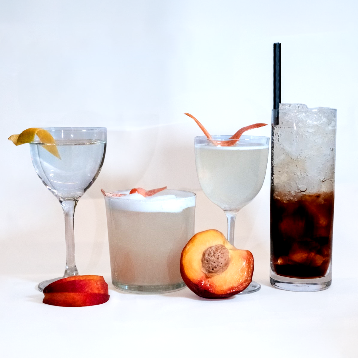 Four Stonefruit cocktails on a white set, with fresh peaches and stone-fruit slices